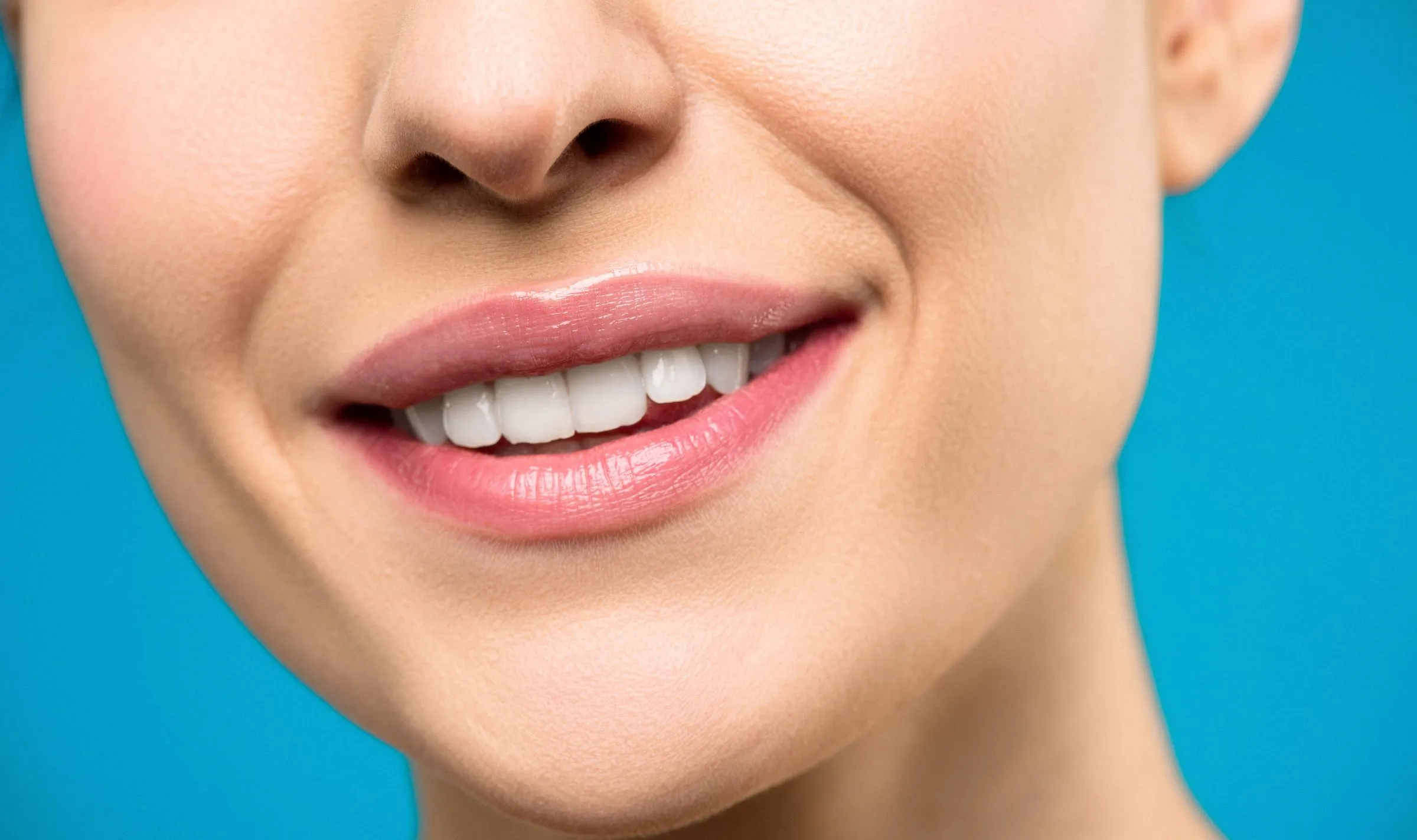 Close-up of a bright, natural smile against a soft aqua background