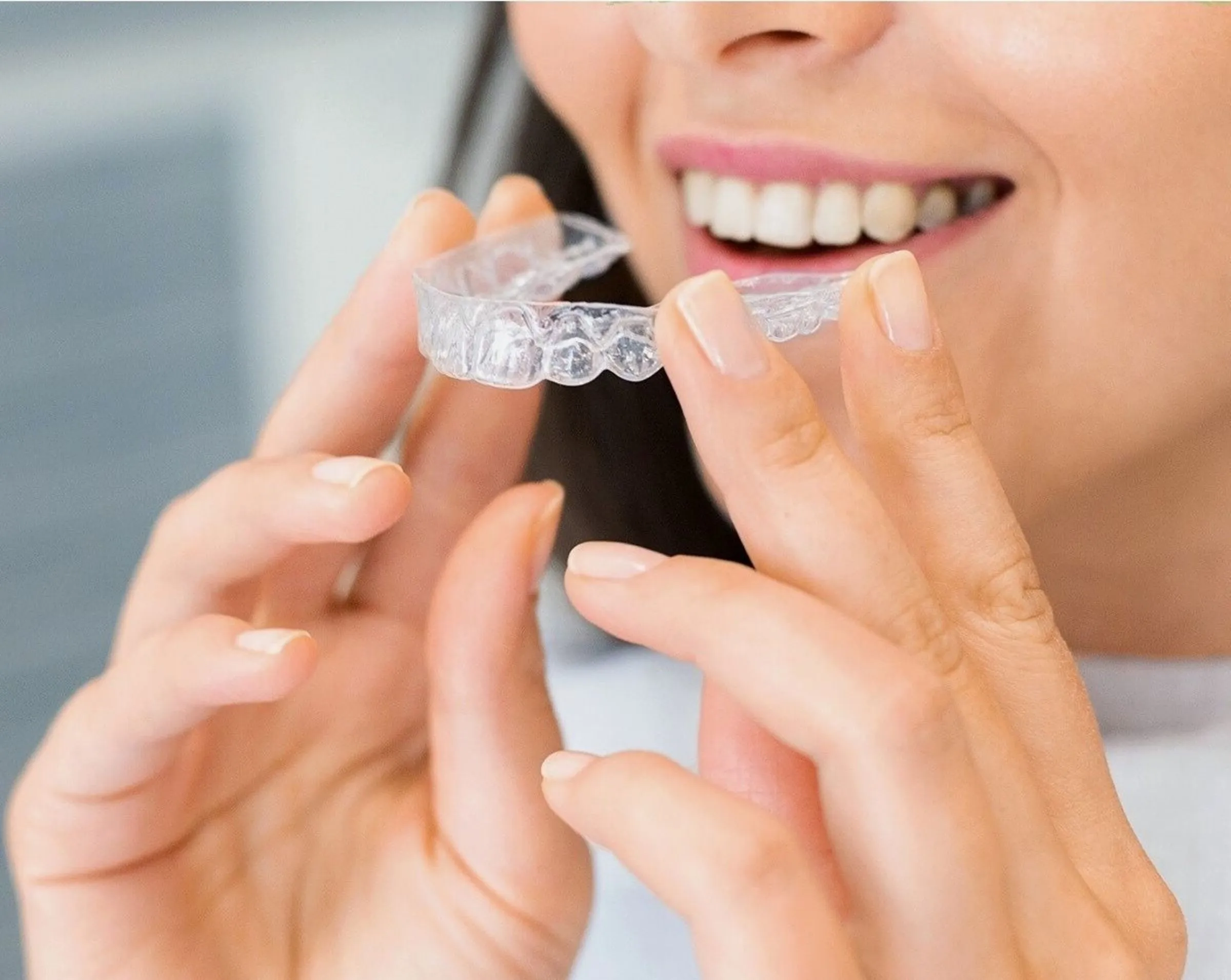 A smiling woman holding a clear aligner tray up to her teeth